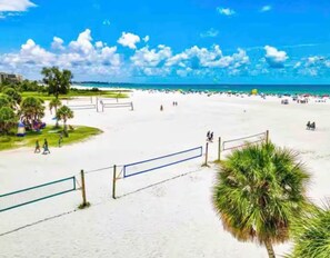 A beach with a volleyball net, palm trees, and a clear blue sky.