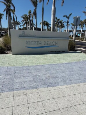 Schild für Siesta Beach, ein Park des Sarasota County, mit blauem Himmel und Palmen im Hintergrund.