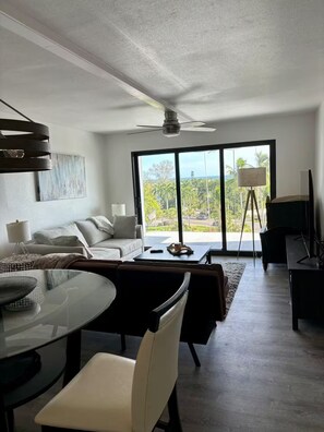 Ein modernes Wohnzimmer mit Glastür zum Balkon, Deckenventilator und Essbereich mit Glastisch.