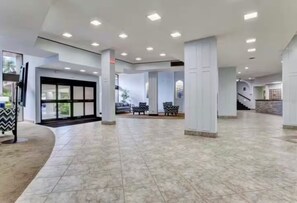 A spacious lobby with a high ceiling, recessed lighting, and a tiled floor.
