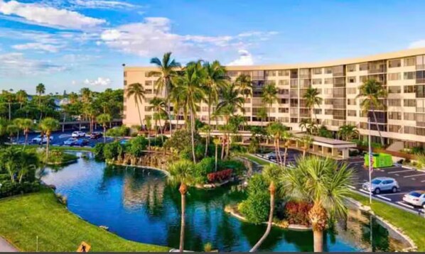 A hotel with a swimming pool, palm trees, and a parking lot.