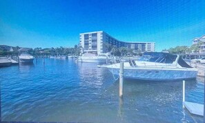 A marina with boats docked, a building in the background, and calm water.