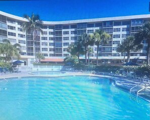 A hotel with a large swimming pool, palm trees, and a multi-story building with balconies.