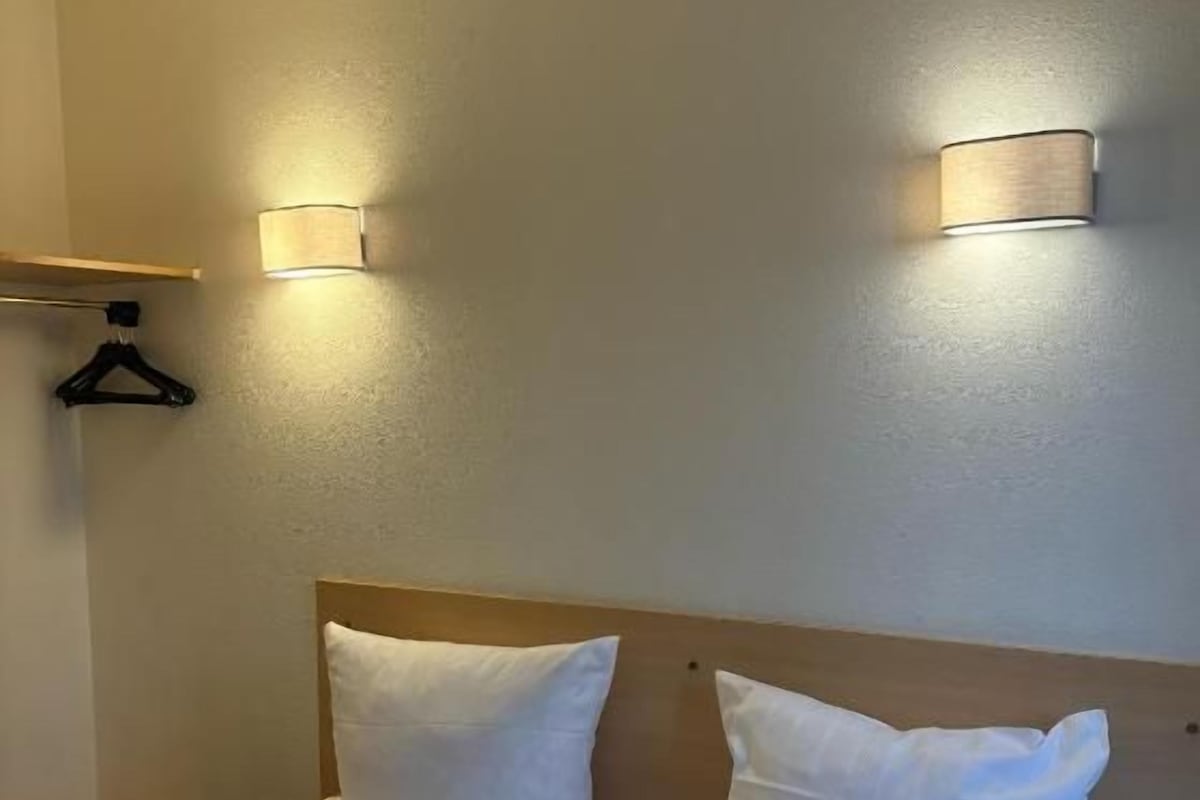 Ein Hotelzimmer mit einem Bett, zwei Wandleuchten und einem hölzernen Kopfteil.