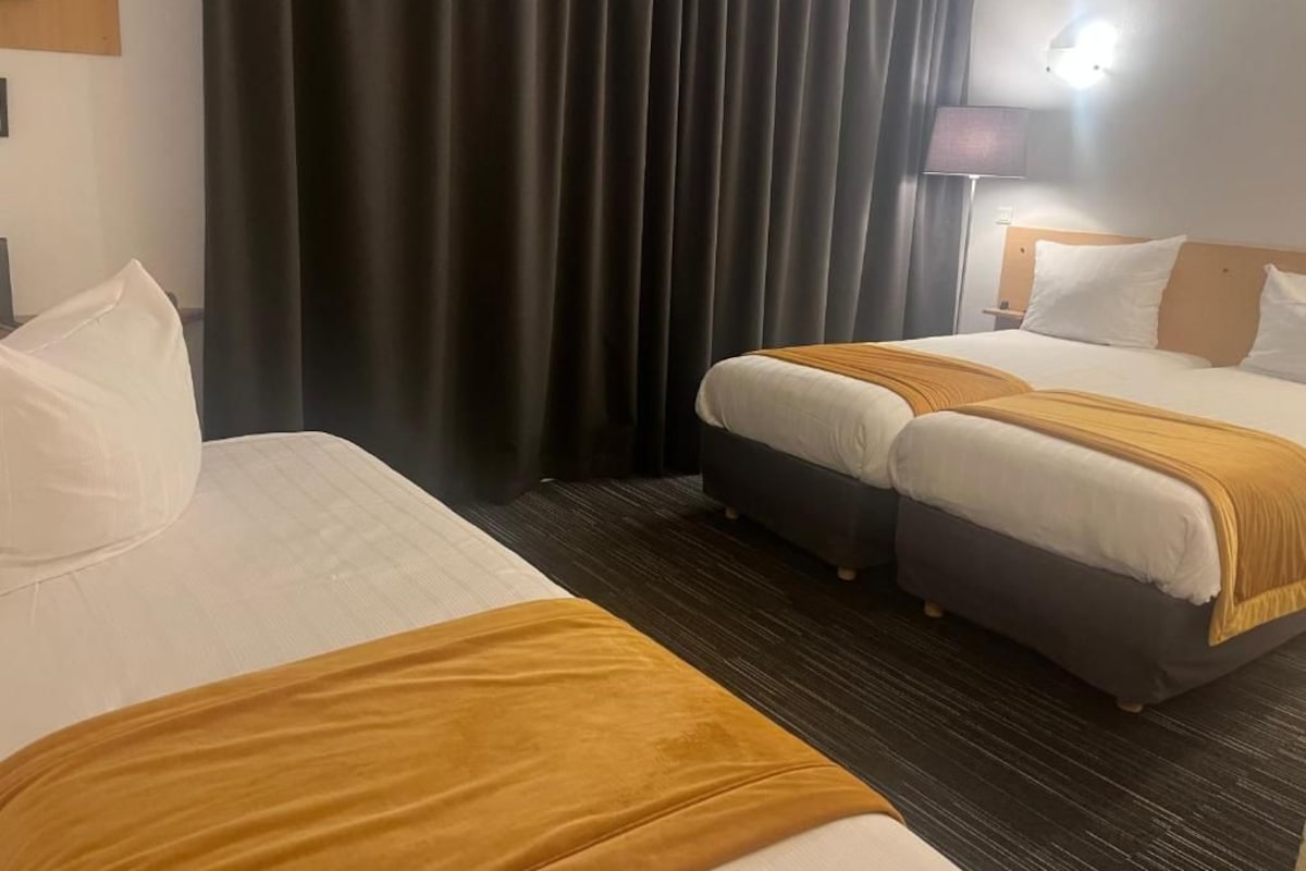 Ein Hotelzimmer mit einem Bett, zwei Nachttischen, einer Lampe und einem fensterbepften Fenster.