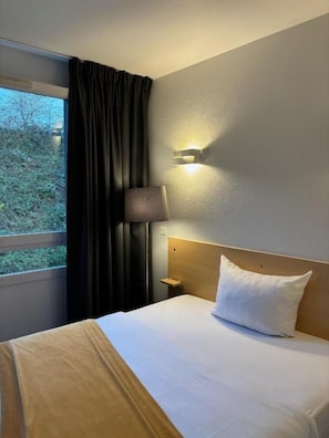 Ein Hotelzimmer mit einem Bett, einem Nachttisch, einer Lampe und einem Vorhangfenster.