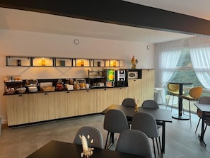 Eine moderne Küche mit integriertem Mikrowellenherd, einer Kaffeemaschine und einem Kühlschrank. Im angrenzenden Bereich befinden sich mehrere Stühle und ein Esstisch.