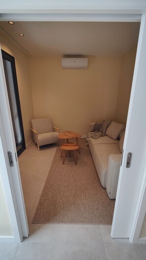 A compact living space with a sofa, a small wooden table, and a ceiling-mounted air conditioning unit.