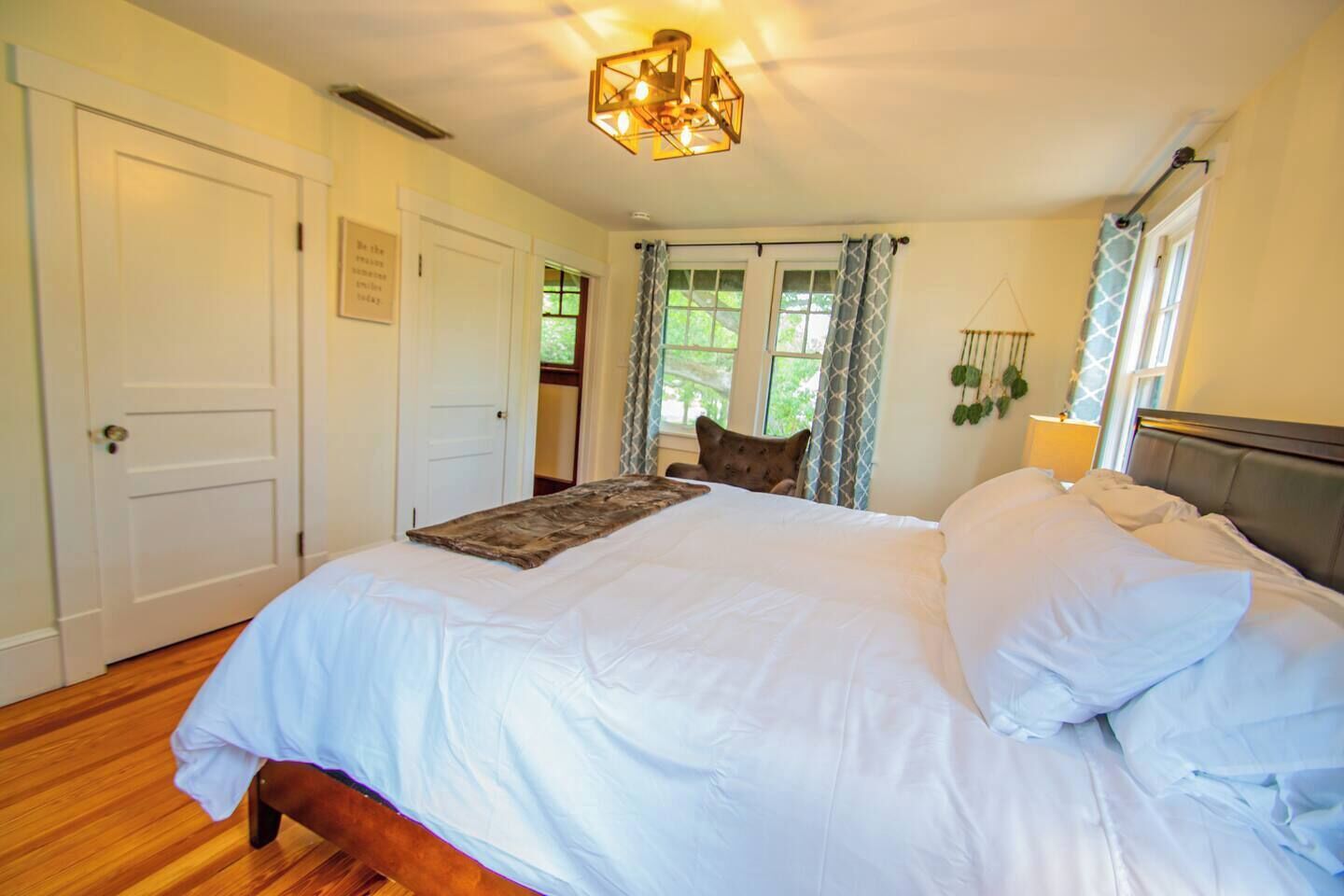 Une chambre à coucher avec un grand lit, une tête de lit en bois, une table de chevet avec une lampe et une fenêtre avec des rideaux.