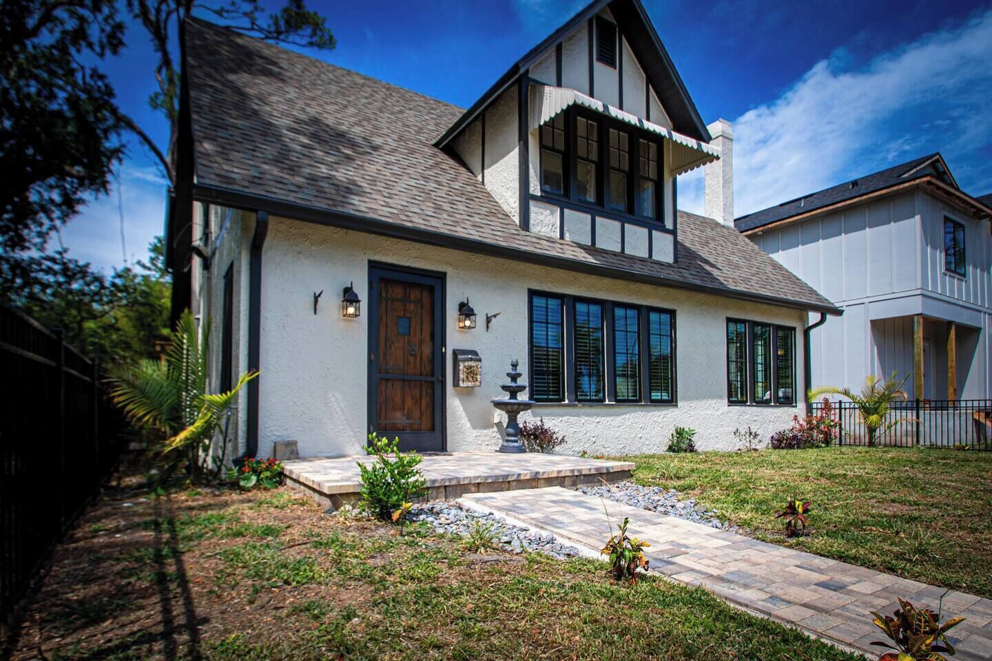 Une maison à deux étages avec une façade en pierre, de grandes fenêtres et un porche à l’avant.