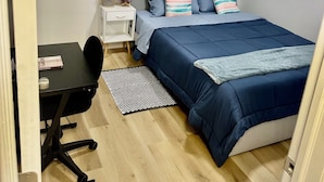Una camera da letto con un letto, una scrivania, una sedia, un tavolino e una mensola a parete.