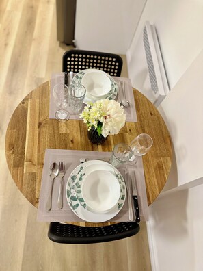 A round wooden dining table with a white and green patterned tablecloth, a vase with white flowers, and a set of cutlery and glasses. - Condo moderne au cœur de Gatineau – À 2mn de A50 et 20 min d'Ottawa (Gatineau)