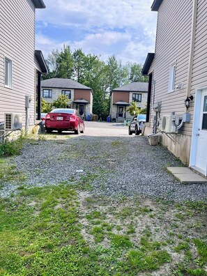 A residential driveway with two cars parked, gravel ground, and houses with similar architecture. - Condo moderne au cœur de Gatineau – À 2mn de A50 et 20 min d'Ottawa (Gatineau)