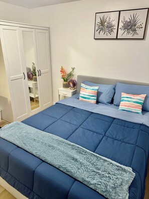 Ein Schlafzimmer mit Bett, Kissen, Nachttisch, einem an der Wand befestigten Bild und einem Kleiderschrank.