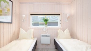 Ein Zimmer mit zwei Betten, einem Fenster mit Blick auf ein Gebäude, einer Wand-Klimaanlage und einem gerahmten Bild an der Wand.