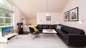 Ein modernes Wohnzimmer mit einer Eckcouch, einem Fernseher, einem Kamin und großen Fenstern.