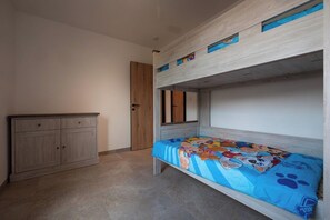 A bunk bed with a blue bedspread featuring cartoon characters, a wooden wardrobe, and a door in a room with tiled flooring. - Klein Lauw 39 in calm area of Haspengouw (Tongeren-Borgloon)