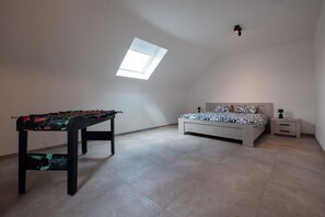 Ein Zimmer mit einem Kicker, einem Bett mit gemusterten Textilien, einem Nachttisch und einem Oberlicht.