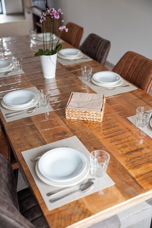 A dining table set with white plates, silverware, and clear glasses, with a woven basket centerpiece. - Klein Lauw 39 in calm area of Haspengouw (Tongeren-Borgloon)
