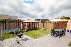 Ein Garten mit Grill, Gartenmöbeln, Trampolin und Schwimmbecken.