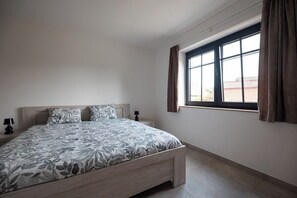Ein Schlafzimmer mit Bett, Nachttisch, einem Fenster mit Vorhängen und Blick ins Freie.