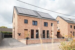 A two-story brick building with solar panels on the roof, a gated entrance, and a small garden area. - Klein Lauw 39 in calm area of Haspengouw (Tongeren-Borgloon)