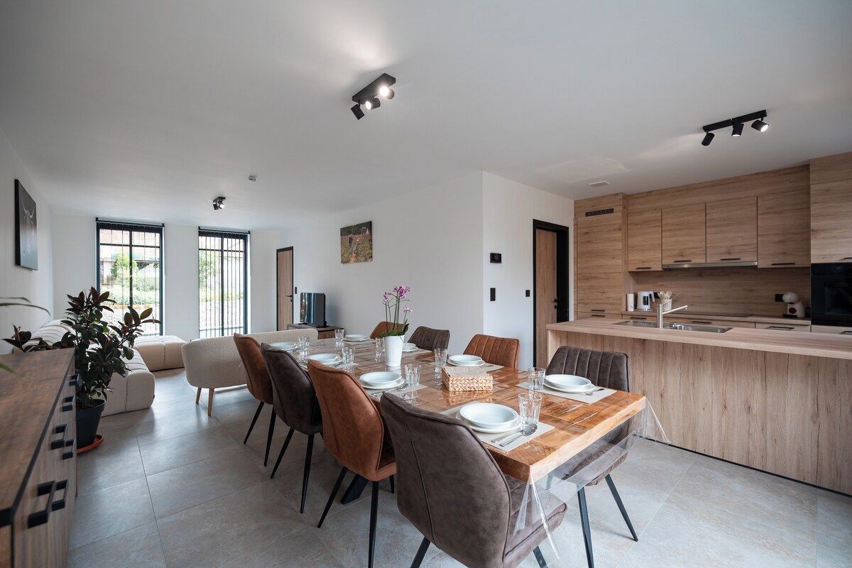 Una cocina moderna con armarios de madera, una zona de comedor con mesa y sillas de madera, y un ventanal que proporciona luz natural.