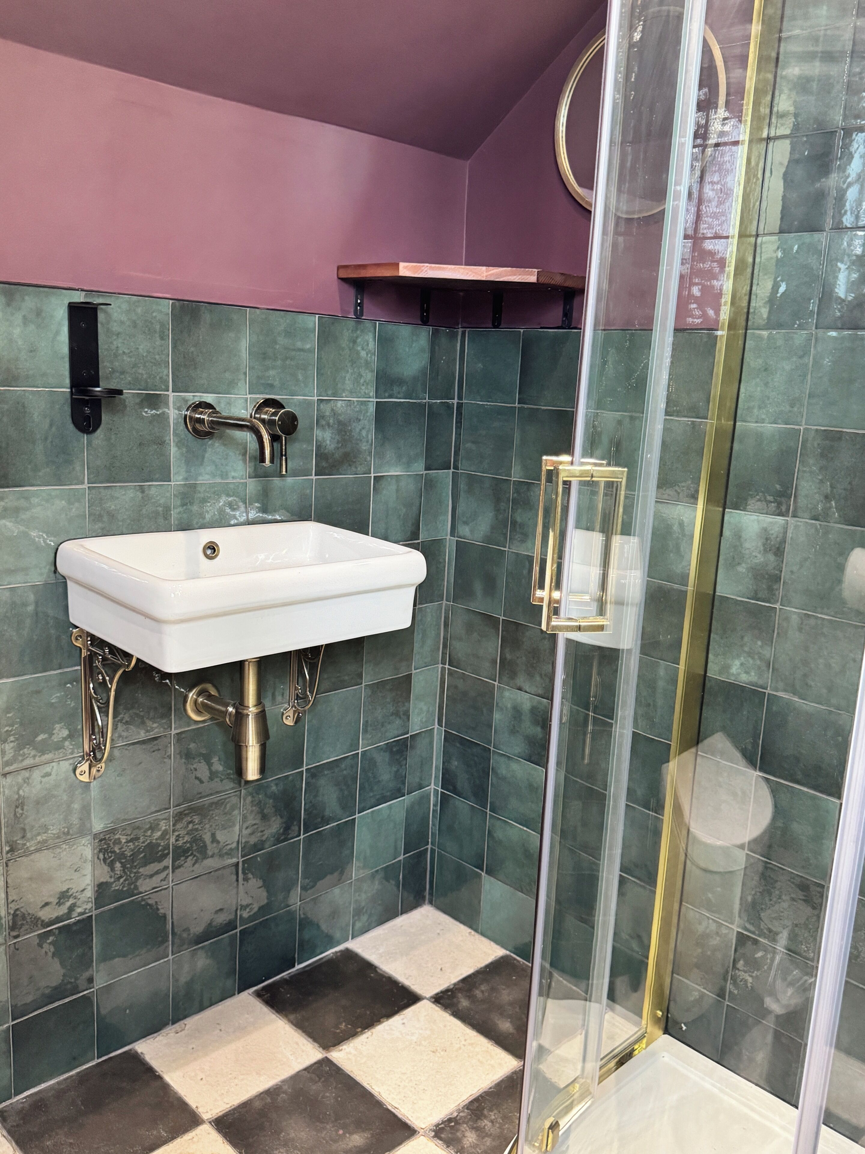 A bathroom with a white sink, green tiles, a glass shower enclosure, and a purple accent wall.