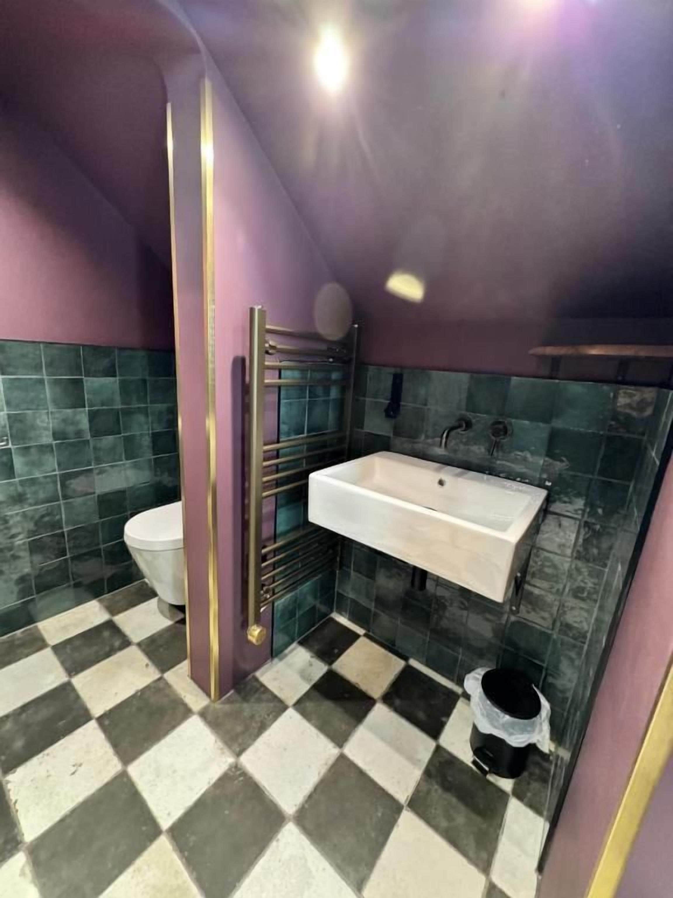 A bathroom with a checkered floor, a white sink, a toilet, and a shower area.