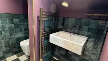 Une salle de bain avec un carrelage à motifs géométriques, un lavabo blanc, des toilettes et un espace douche.
