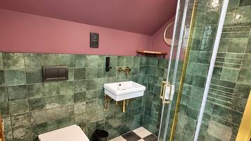 Un baño con piso de cuadros, inodoro blanco, lavamanos y ducha con cerramiento de vidrio.
