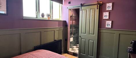 Un dormitorio con una cama, una ventana, un radiador, una puerta y una lámpara en el techo.