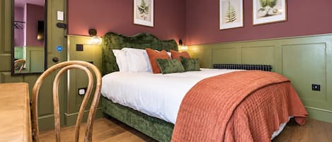 Une chambre à coucher comprenant un lit, une chaise, un radiateur et des reproductions encadrées de motifs botaniques accrochées au mur.