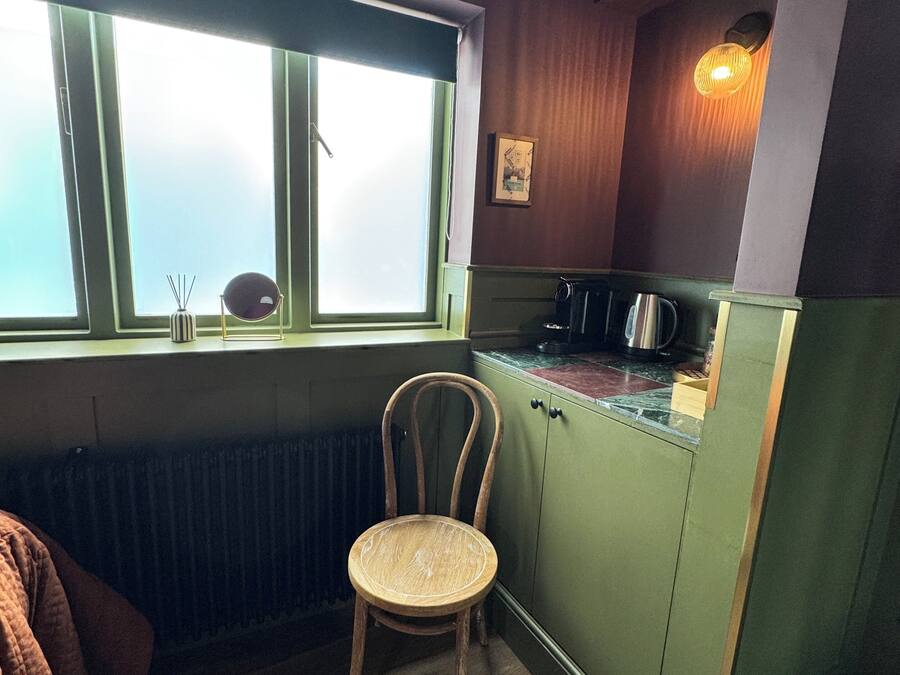 A small kitchen with a window, a chair, and a radiator.