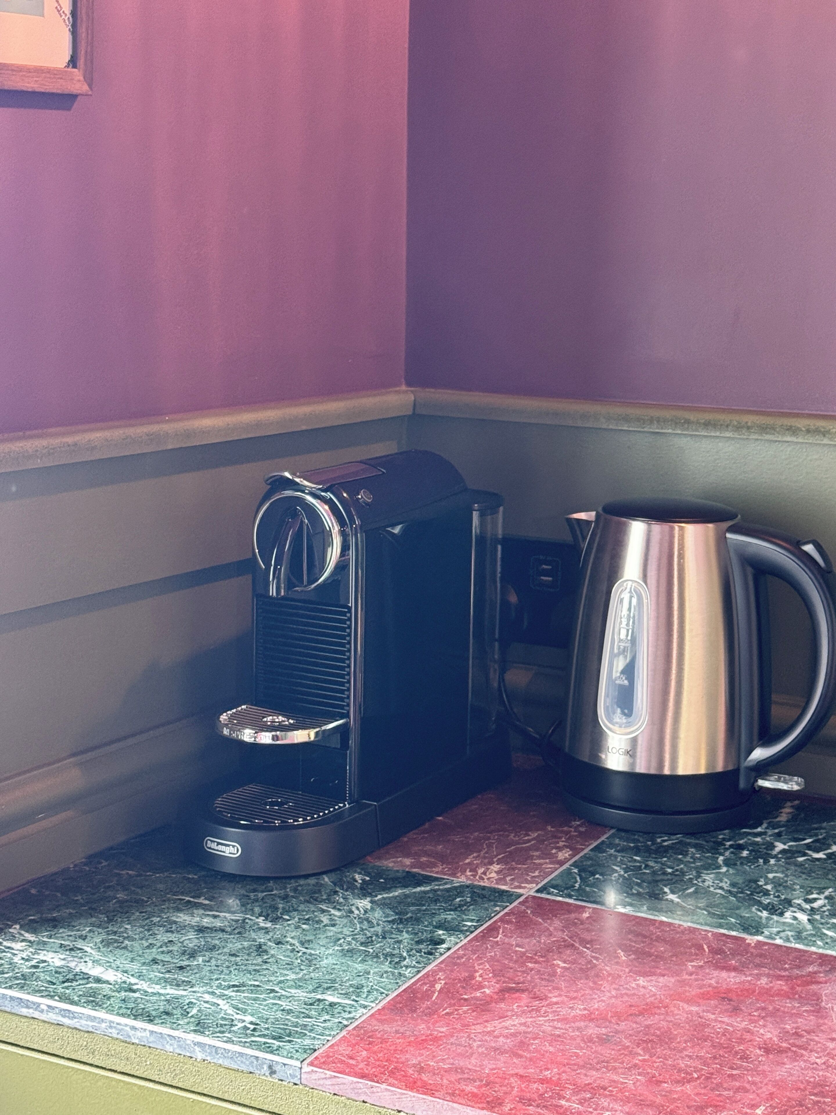 A kitchen area with a coffee maker and a kettle on a countertop.