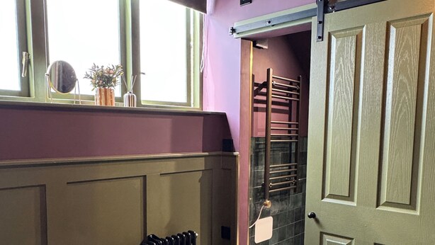 A room with a radiator, a bed, a window with a view, and a door leading to a staircase. - The Linen Rooms (Knutsford)