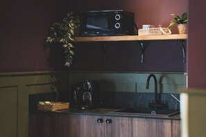 A kitchen with a microwave on a shelf, a coffee maker, and a sink. - The Linen Rooms (Knutsford)