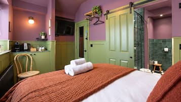 Een hotelkamer met een bed, een stoel, een klein tafeltje, een groene deur, een douchegedeelte en een kitchenette.