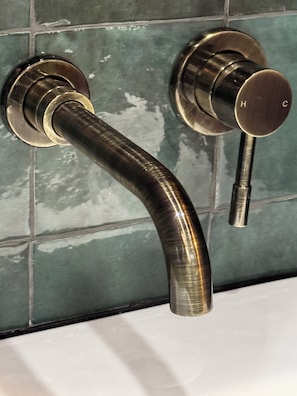 Un baño con un grifo metálico curvado y una llave de control en la pared.