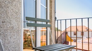 Ein Balkon mit Metallgeländer, einer Holzbank und einem Gebäude mit weißer Fassade im Hintergrund.