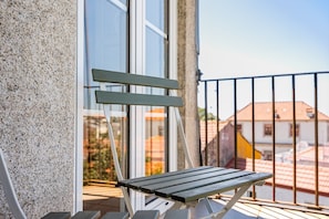 Ein Balkon mit Metallgeländer, einer Holzbank und einem Gebäude mit weißer Fassade im Hintergrund.