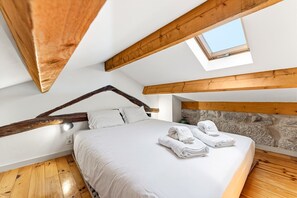 Um quarto com teto inclinado, um claraboia, uma cama com roupa de cama branca e vigas de madeira.