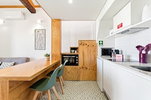 A compact kitchen with a wooden table, chairs, a microwave, and a refrigerator. - GuestReady-Cosy Studio with Balcony in Porto (Porto)