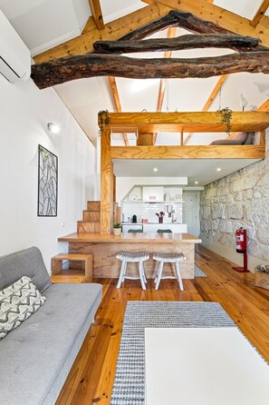 A modern interior with a wooden ceiling, a kitchen area, and a seating area with a sofa and stools.