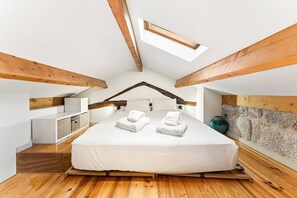 A bedroom with a sloped ceiling, wooden beams, a bed with white linens, and a skylight. - GuestReady-Cosy Studio with Balcony in Porto (Porto)