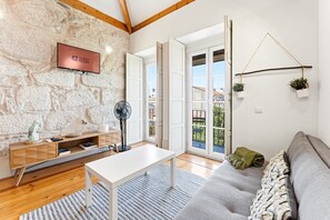 A modern living room with a stone wall, a flat-screen TV, a fan, a sofa, and a view of the outside.