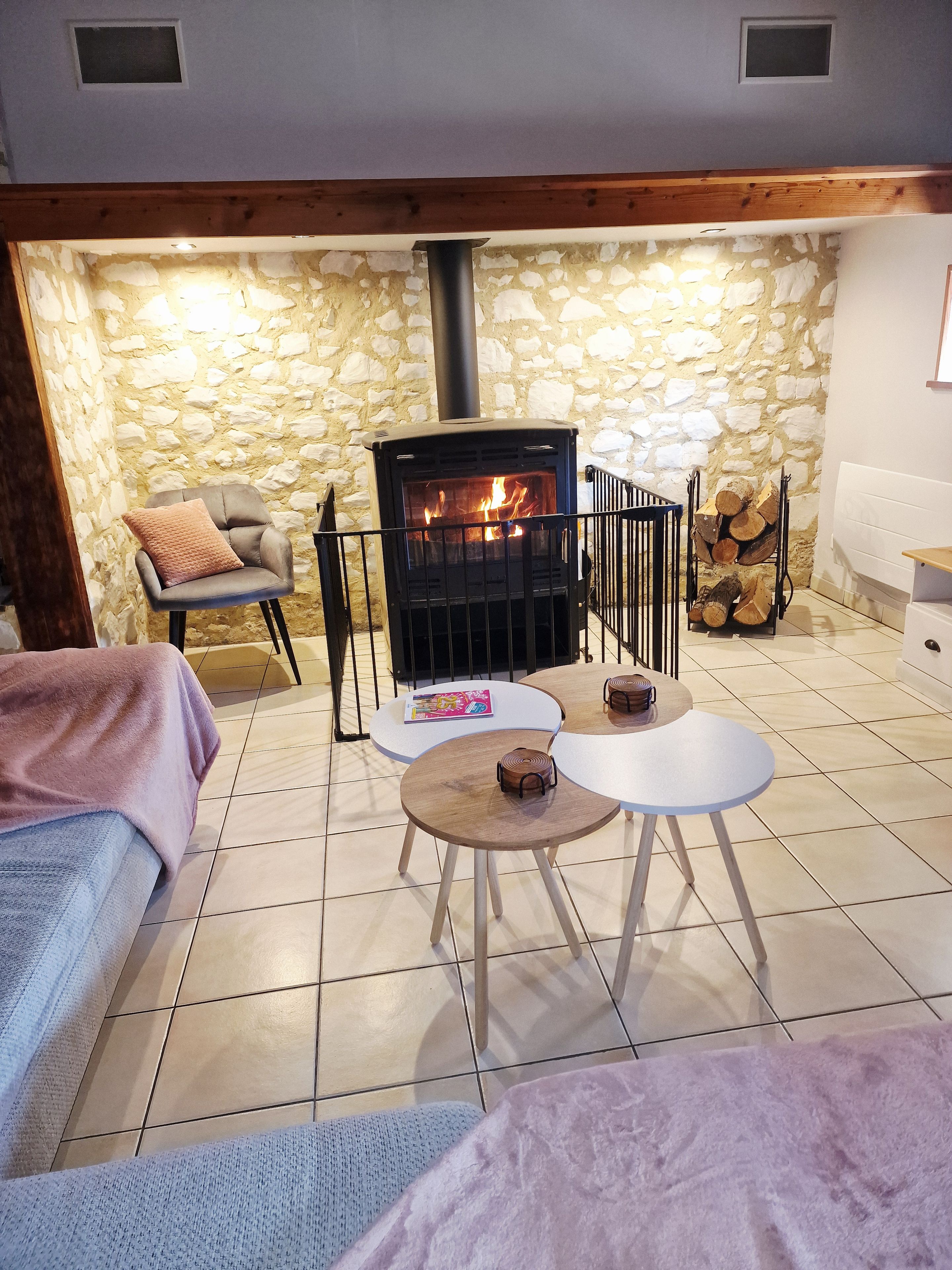 A cozy room with a stone wall, a fireplace, a chair, and a small table.