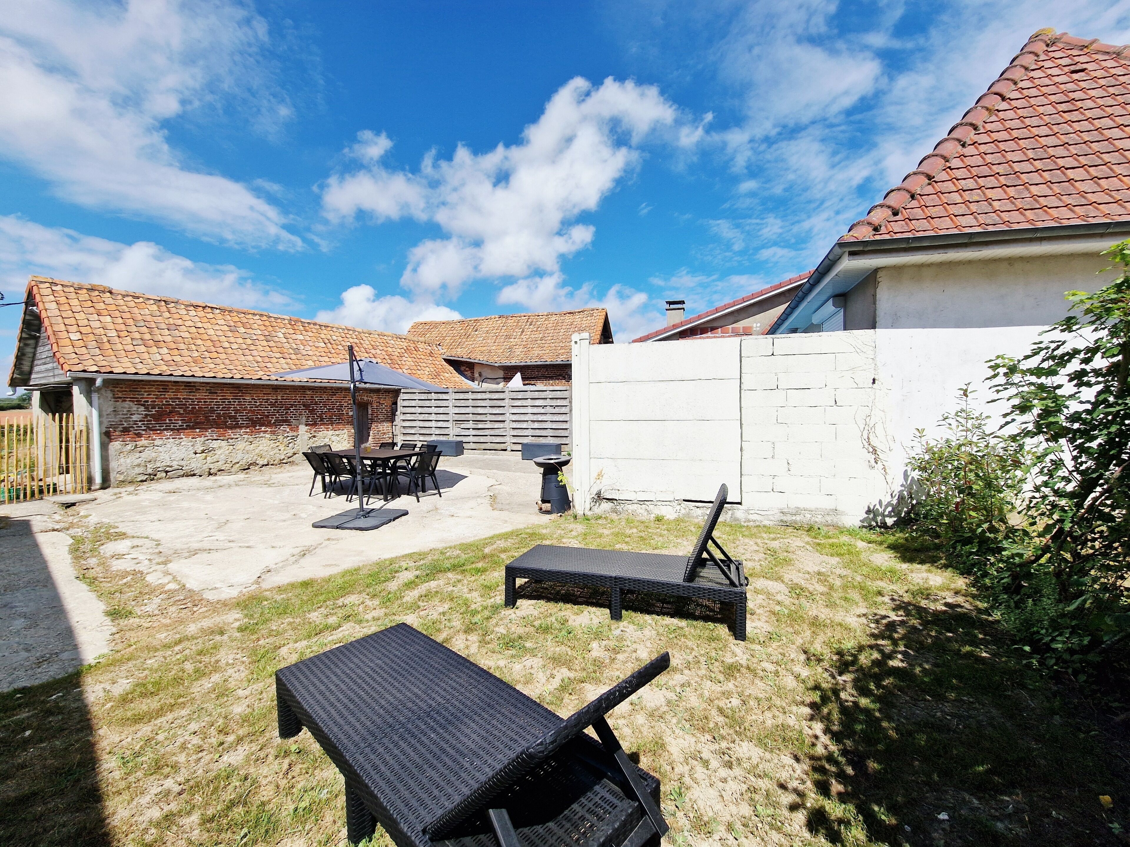 Un jardin avec un espace barbecue, du mobilier d’extérieur et un mur blanc.