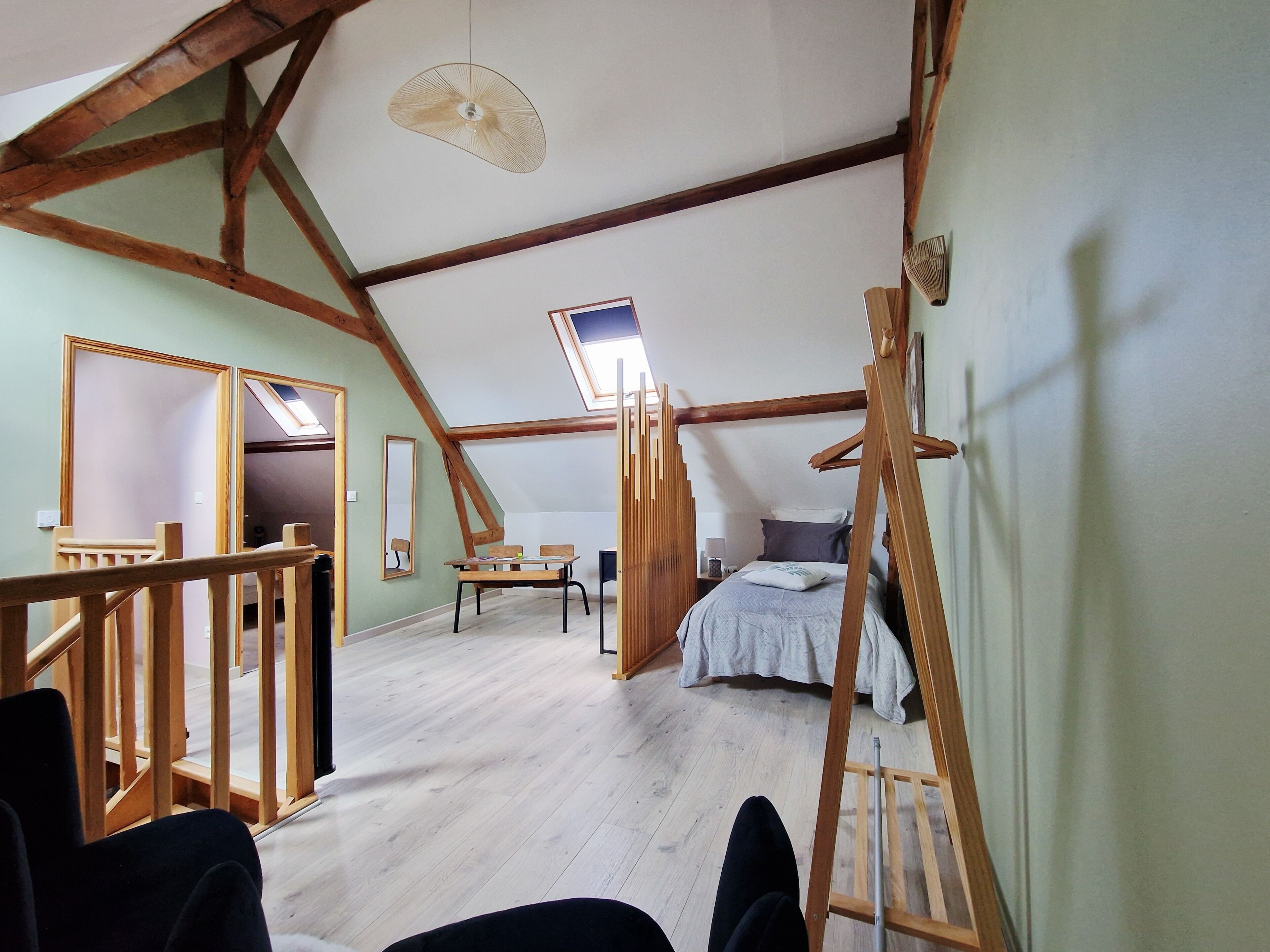 Une pièce avec un plafond en pente, des poutres en bois, un lit, un bureau et une chaise.