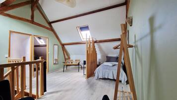 Une pièce avec un plafond en pente, des poutres en bois, un lit, un bureau et une chaise.